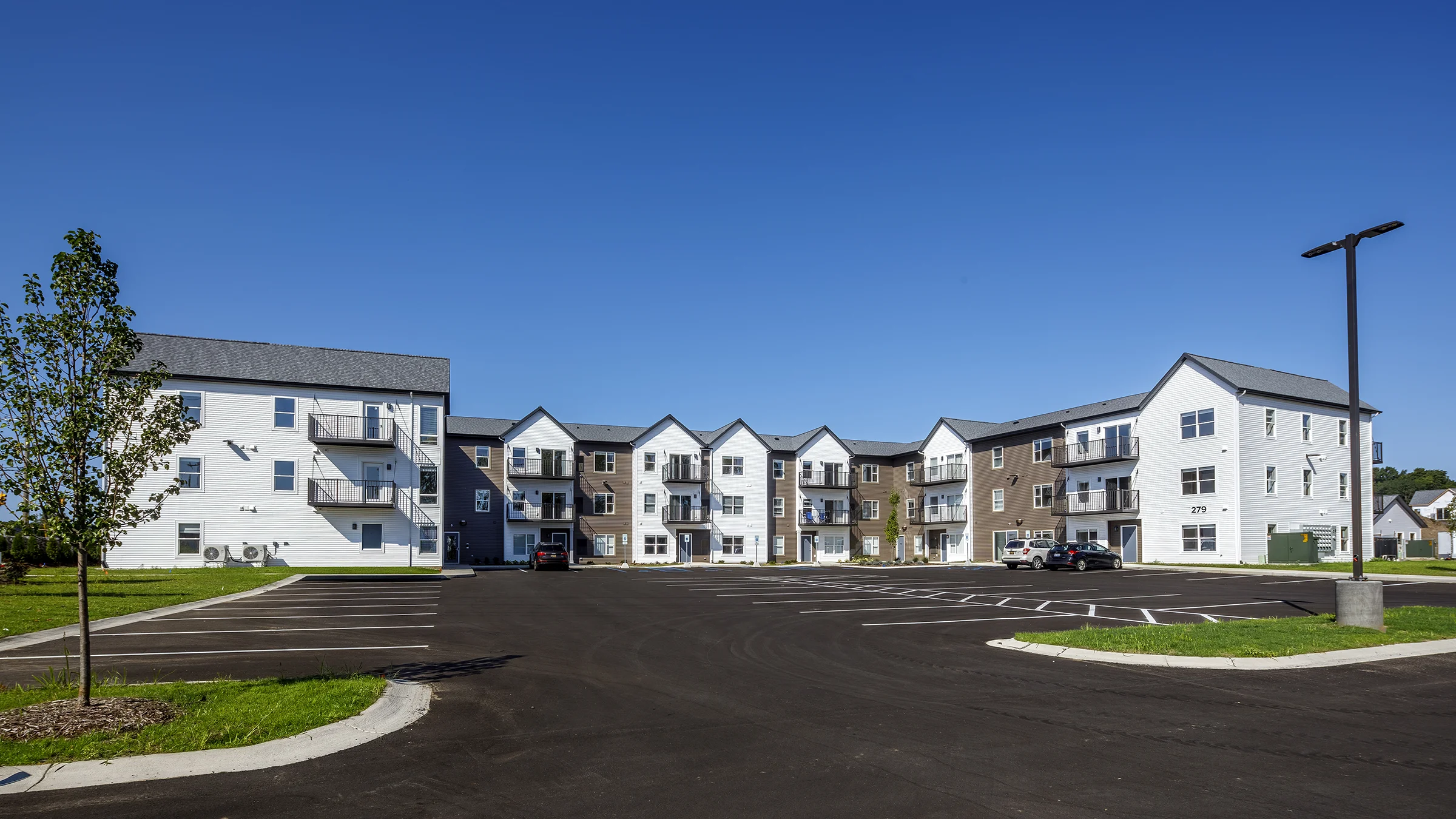 Lakewood Place Apartments with white siding and medium brown brick. Large parking lot adjacent to the apartment complex.