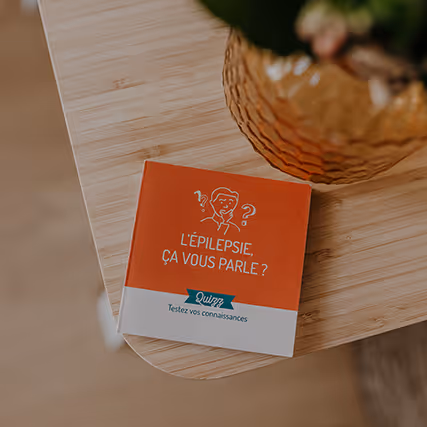 Livret rouge et blanc posé sur un bureau en bois clair, intitulé "L’épilepsie, ça vous parle ? – Testez vos connaissances".