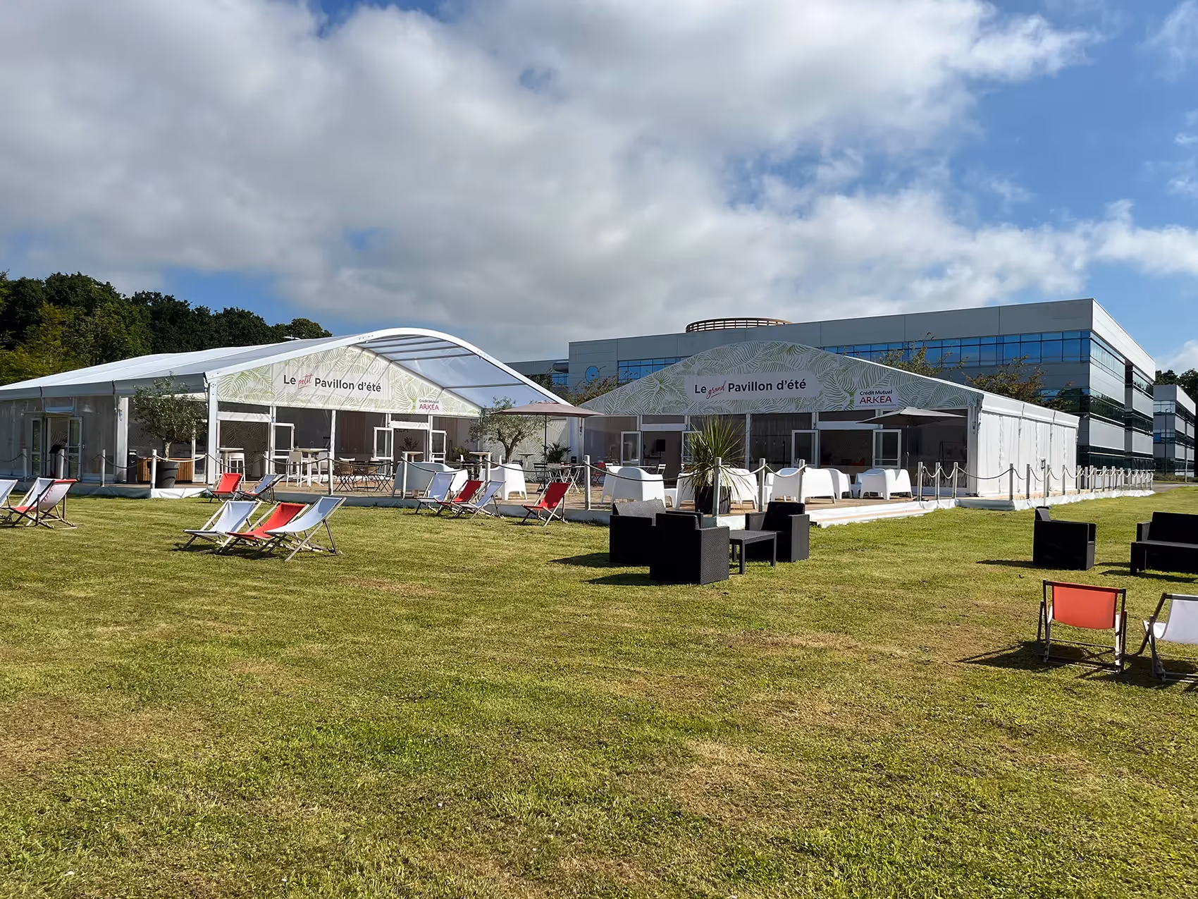Pavillon d'été Arkéa avec transats et tentes blanches sur pelouse, devant un bâtiment moderne vitré.