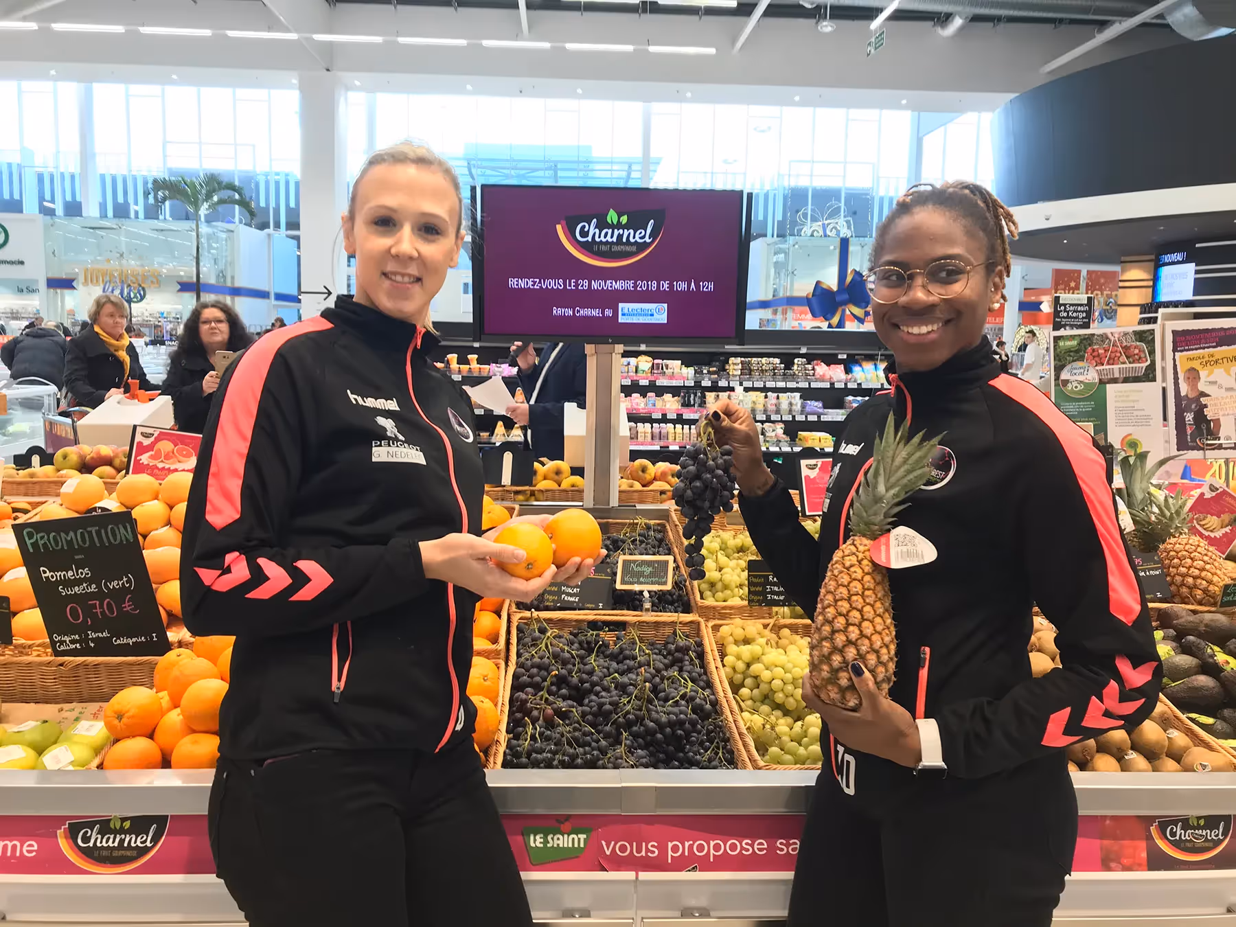 Deux femmes souriantes en tenue sportive tenant des fruits dans un rayon de supermarché Charnel.