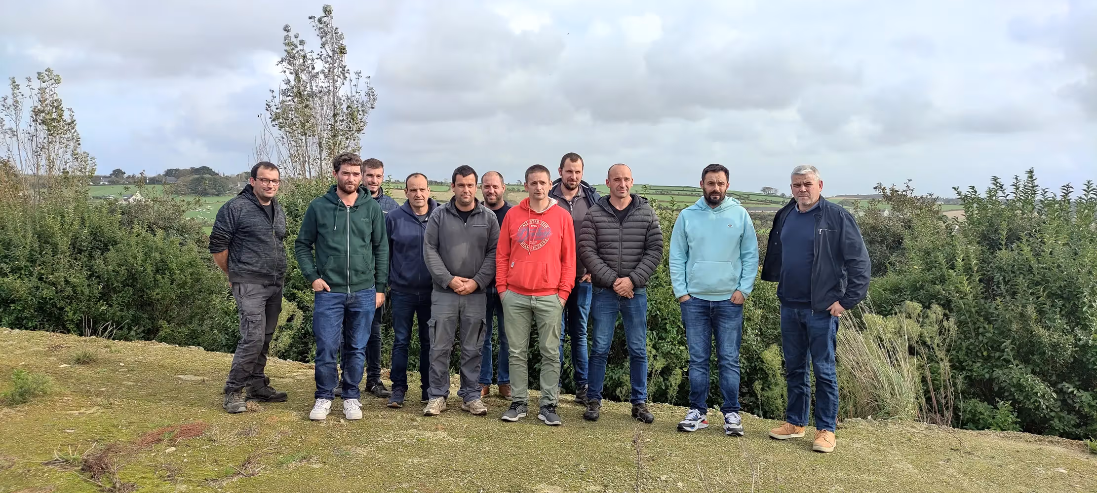 Onze hommes posant ensemble en extérieur devant un paysage agricole, membres du collectif Les Biogaziers.
