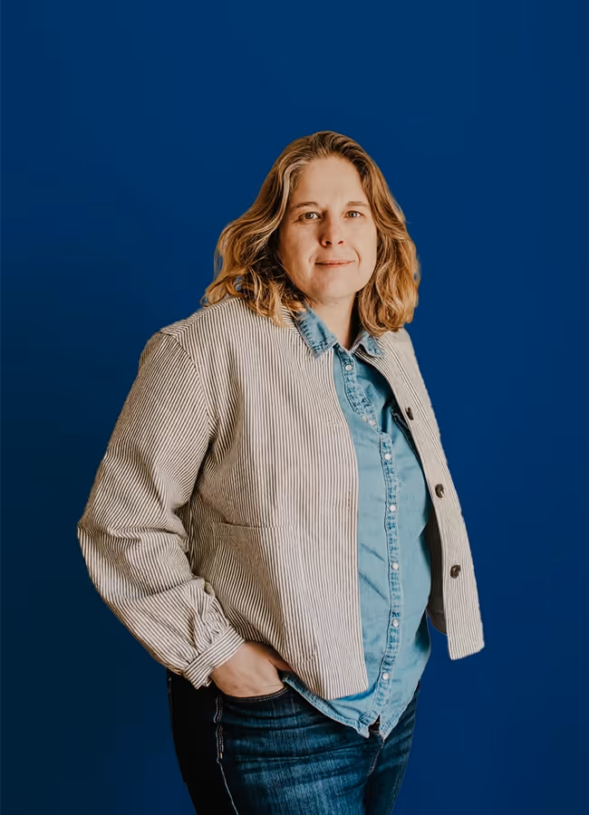 Portrait de Florence en chemise en jean et veste à rayures, les mains dans les poches de son jean foncé.
