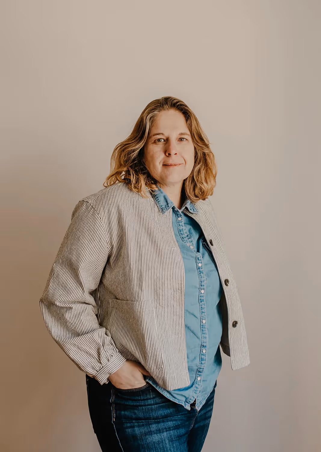 Portrait de Florence en chemise en jean et veste à rayures, les mains dans les poches de son jean foncé.