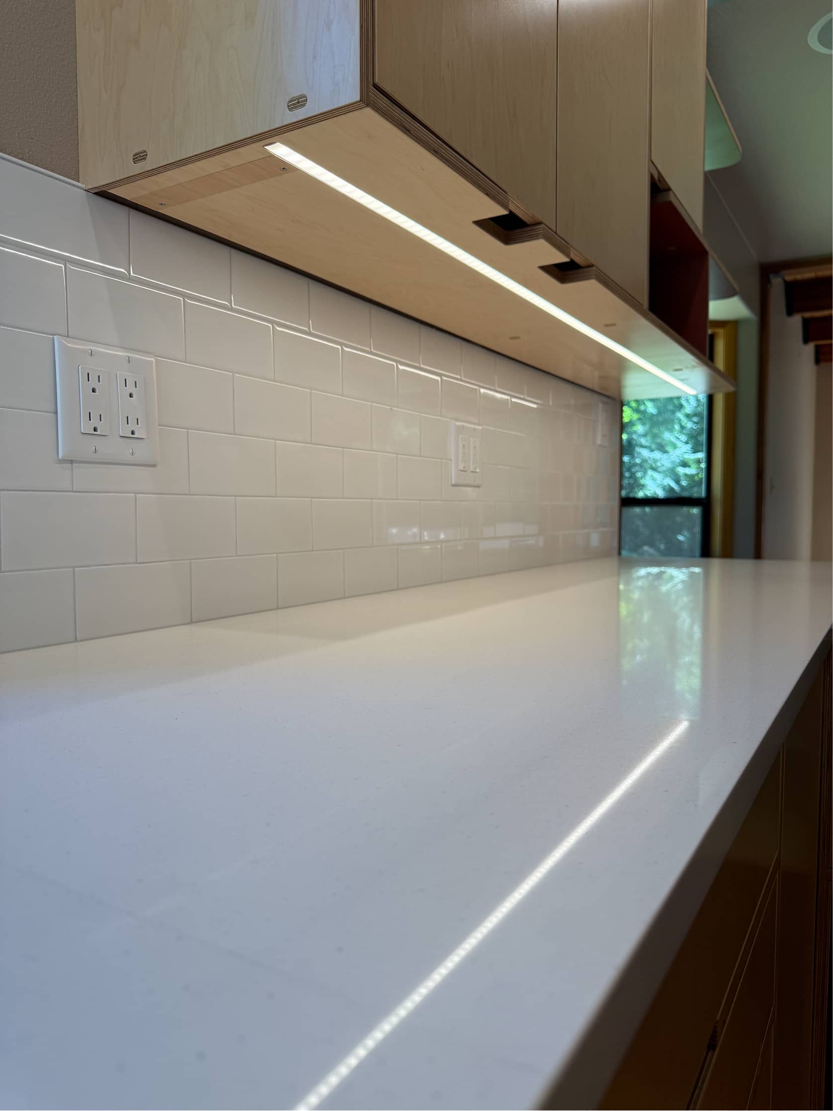 Quartz countertop detail with under-cabinet LED lighting and subway tile by NBE LLC