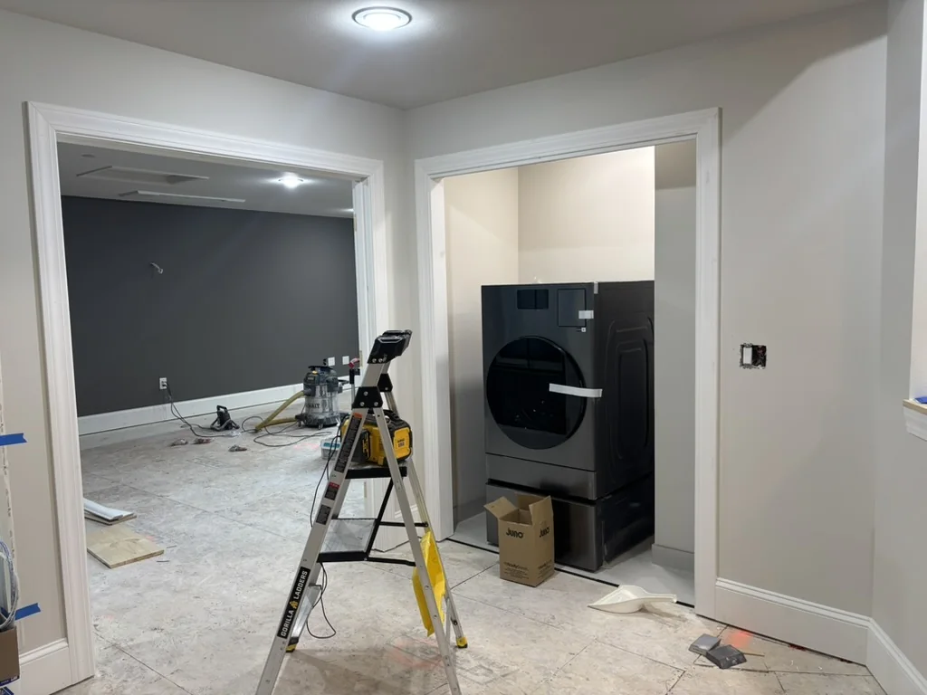 Interior hallway with a black front-loading washer in an alcove, a step ladder, and a doorway leading to a room with gray walls.