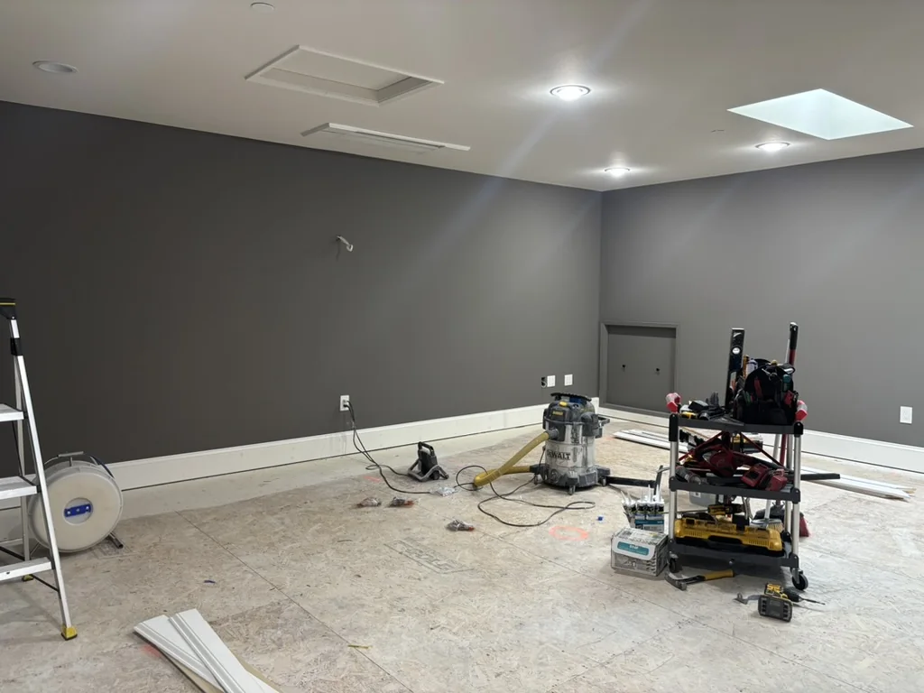Empty interior room with dark gray walls, recessed lighting, concrete floor, and various power tools and equipment scattered around