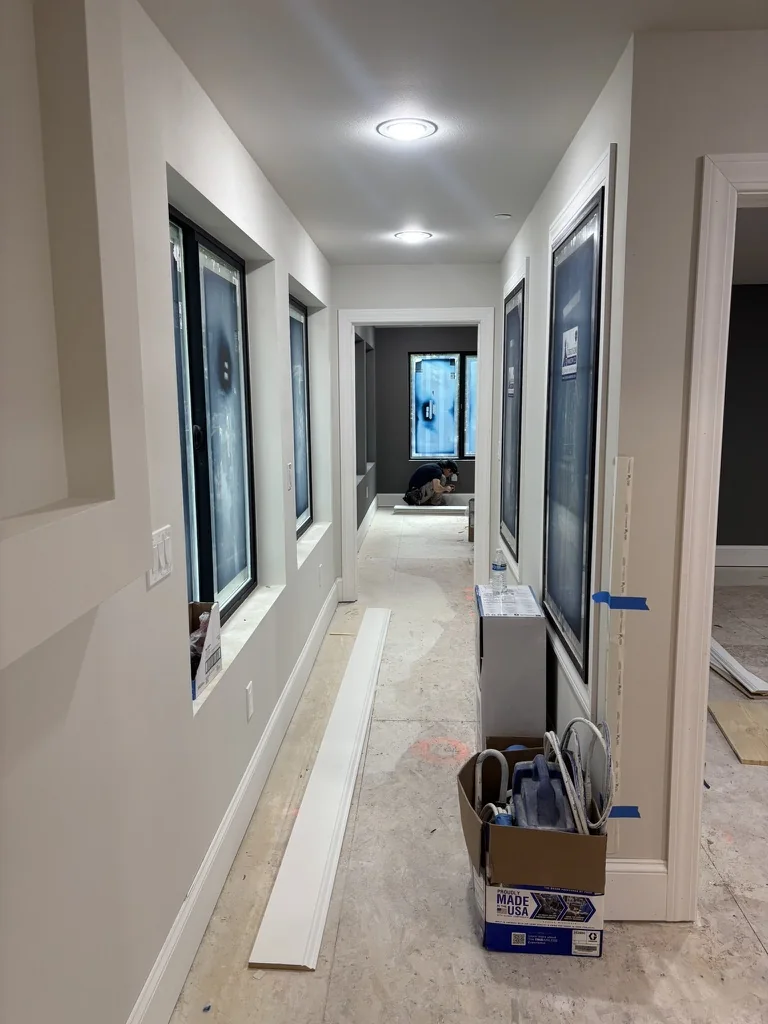 A hallway under renovation with windows, white trim, a person working, and construction materials on the floor