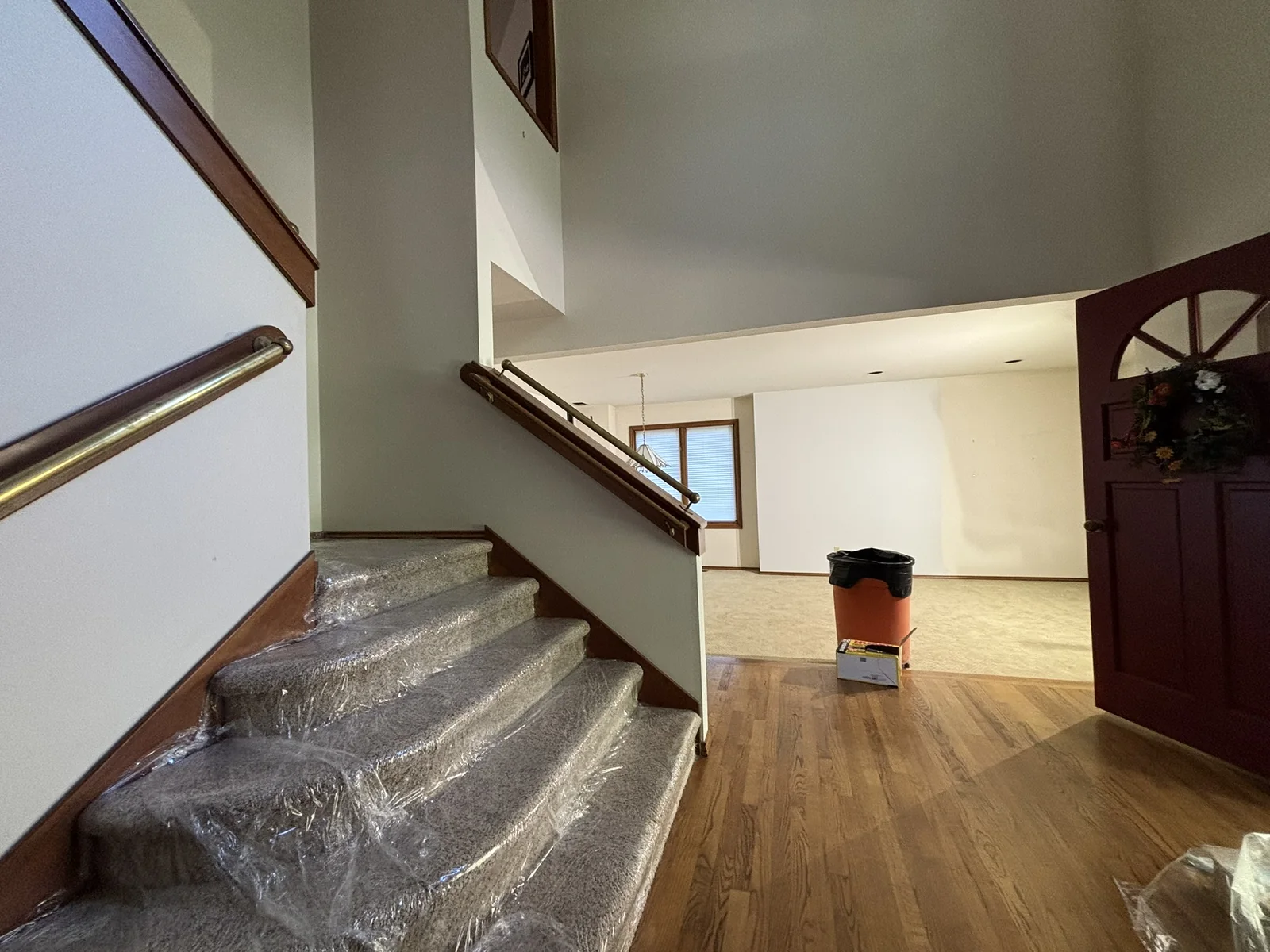 Carpeted stairs wrapped in clear plastic lead beside hardwood flooring into an open room.