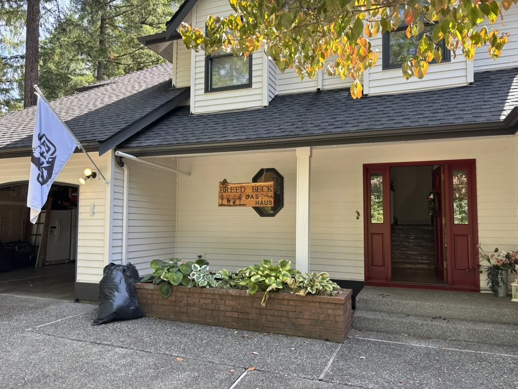 Exterior view of a cream house with a dark roof, red entry door, brick planter, and driveway.