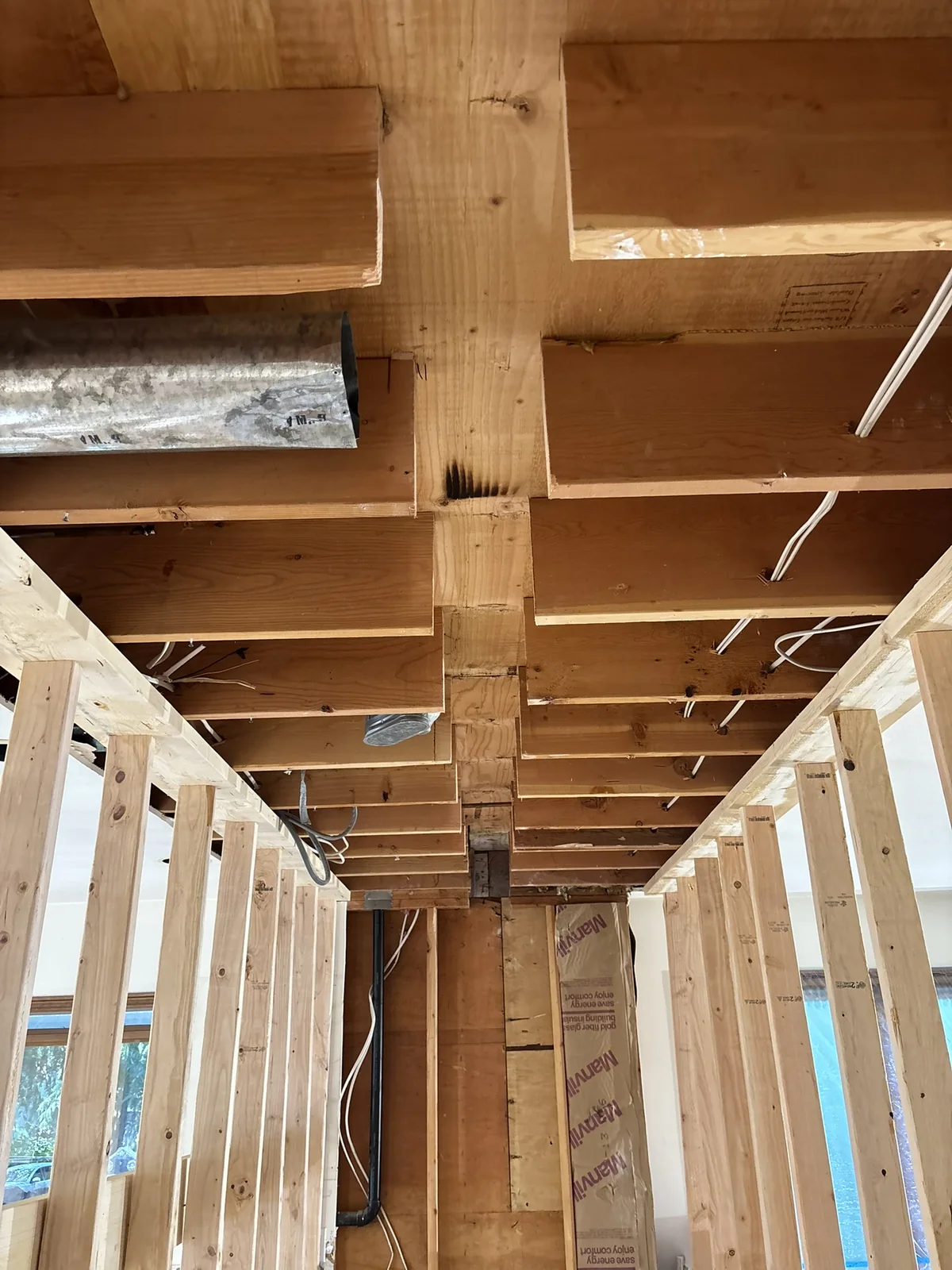 Exposed wood floor joists, wall studs, metal ductwork, electrical cables, and packaged insulation.