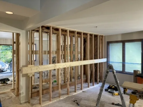 Interior room with exposed wooden wall framing, a long board, ladder, tools, and a window.