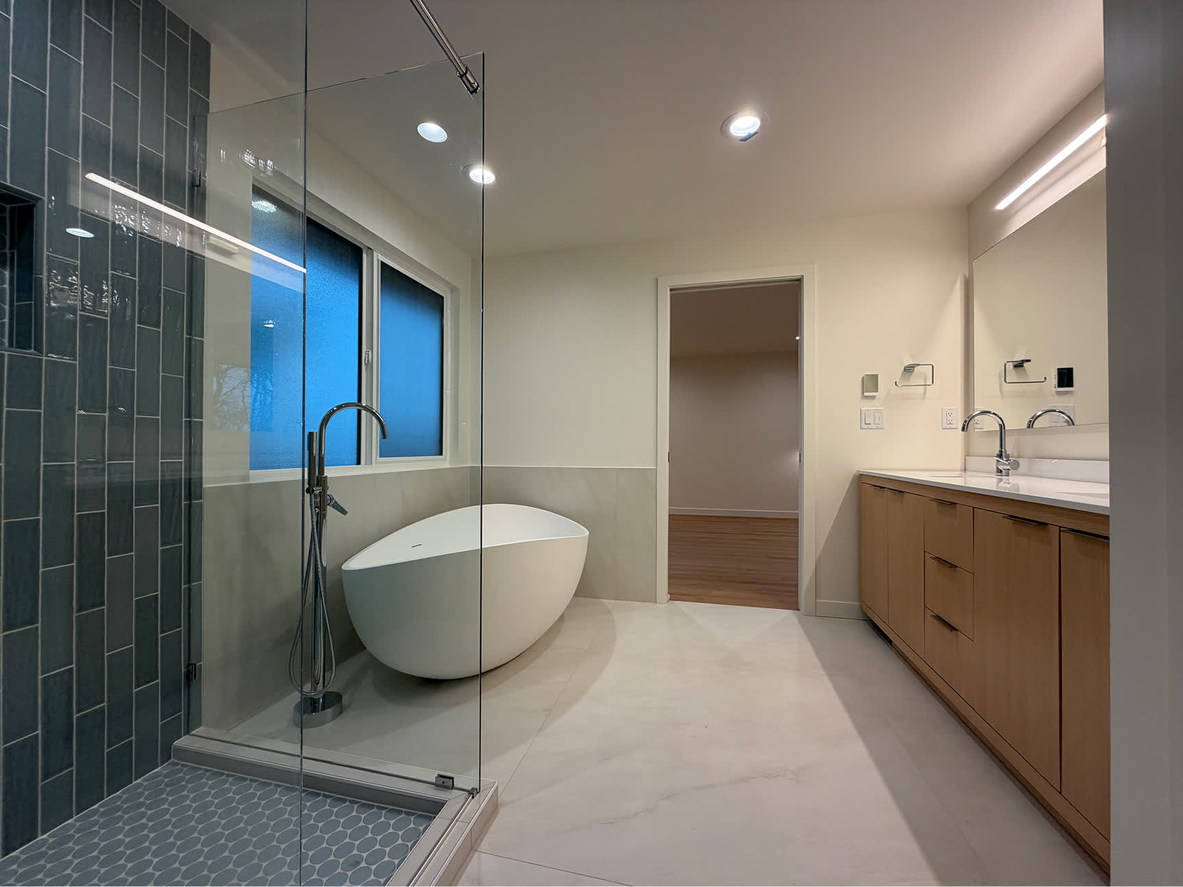 Glass-enclosed tiled shower, freestanding tub and double vanity in NBE LLC’s completed Bellevue bathroom renovation.