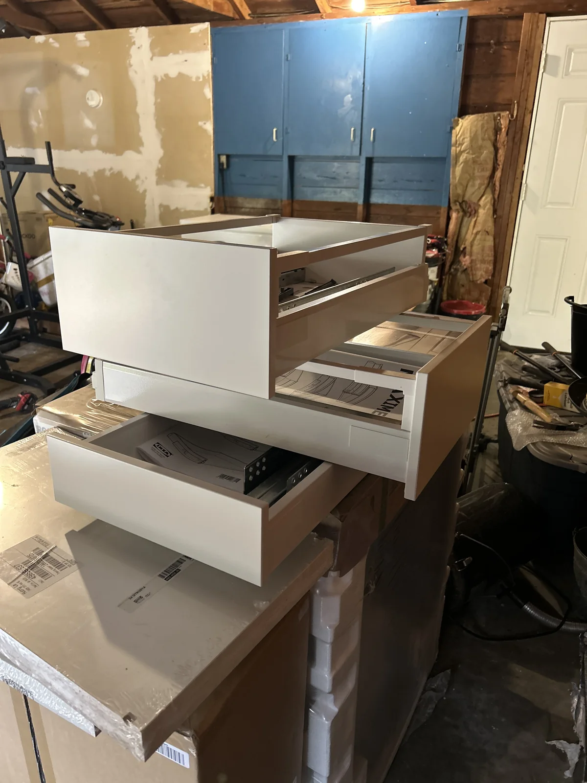 Three white drawer units with open fronts stacked on cardboard boxes in a workshop