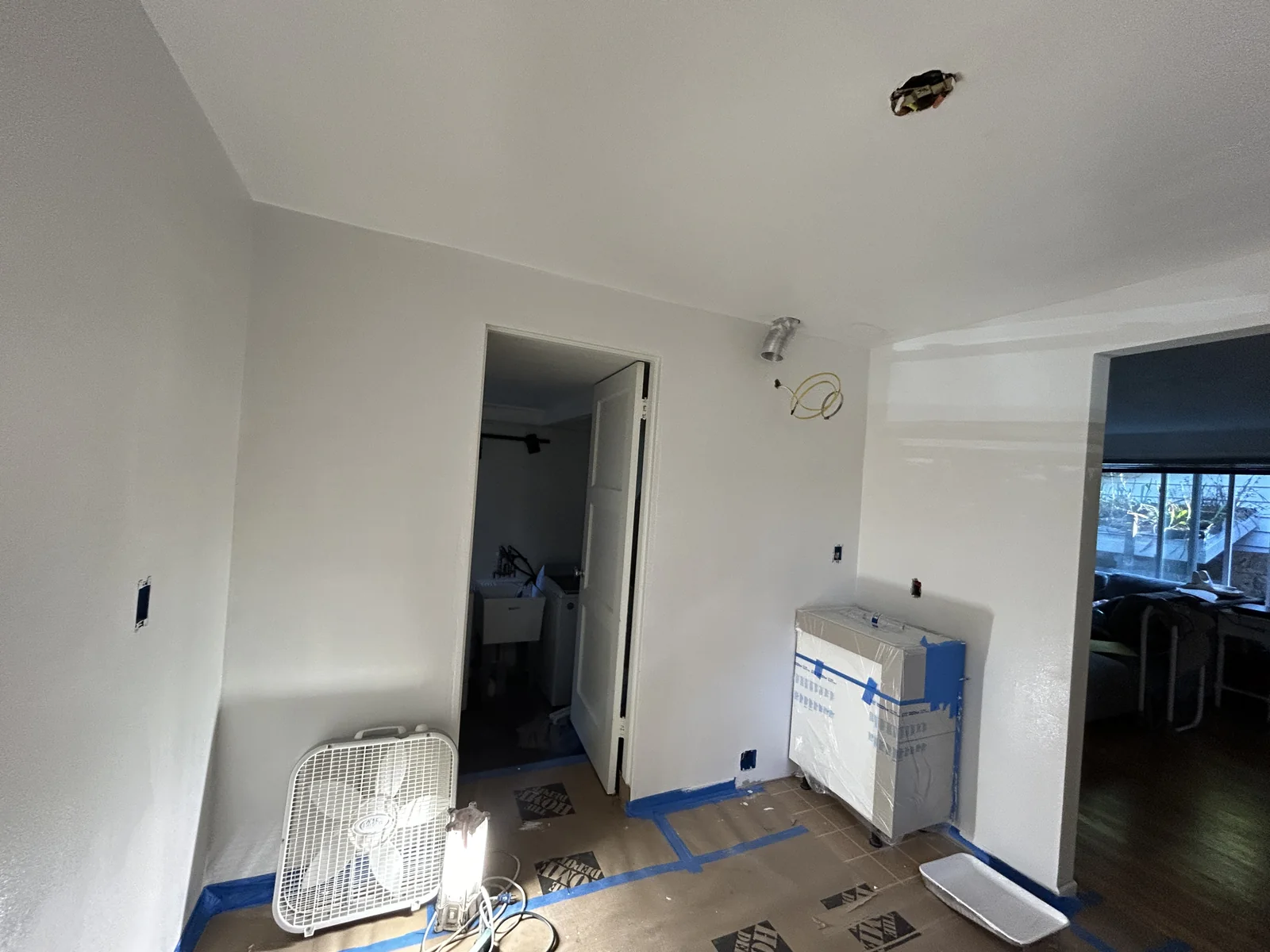 White walls exposed ceiling wiring fan protective floor covering and wrapped appliance in a partially finished room