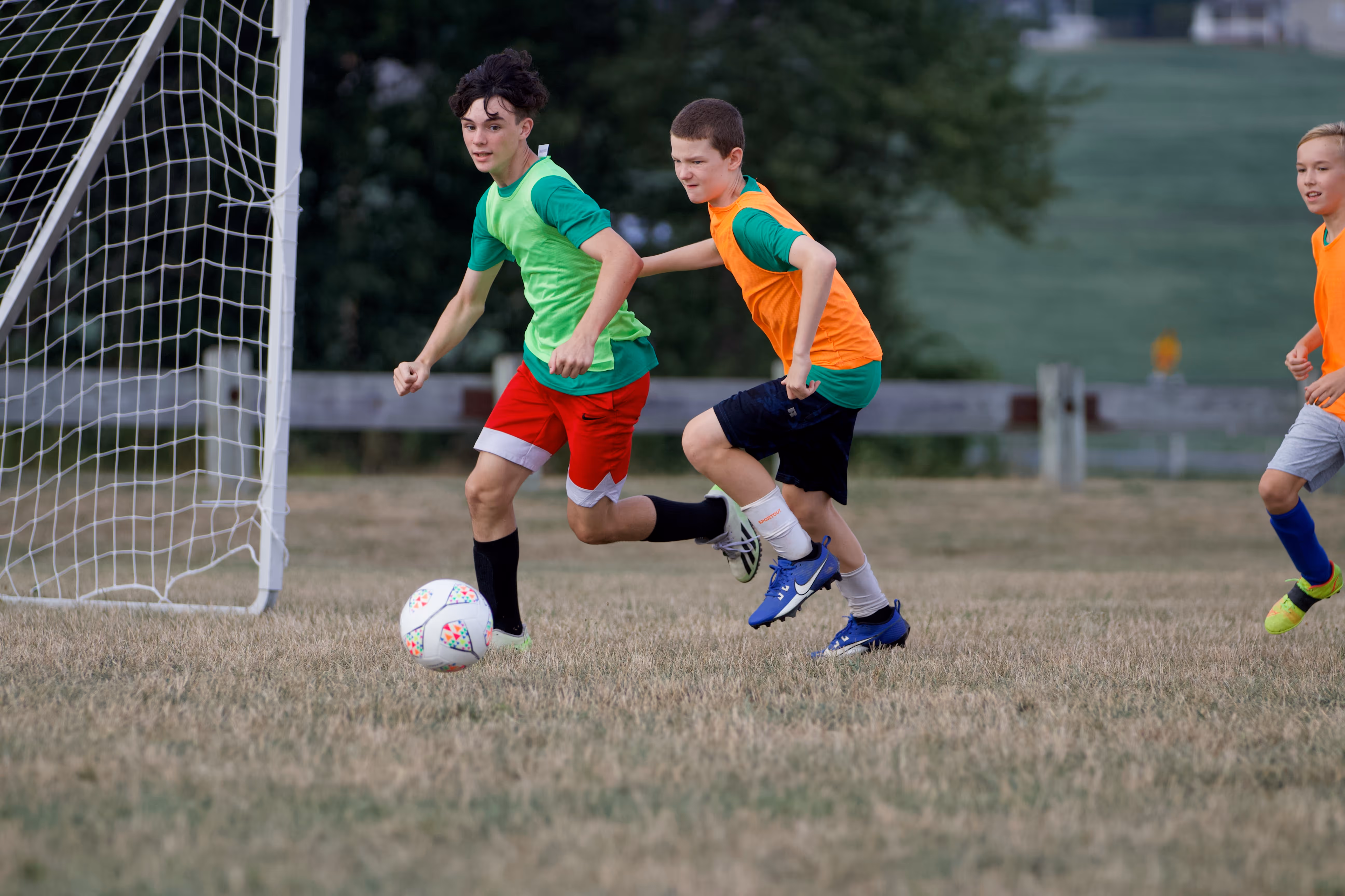 Two young boys playing soccer on a field with other children in the background.