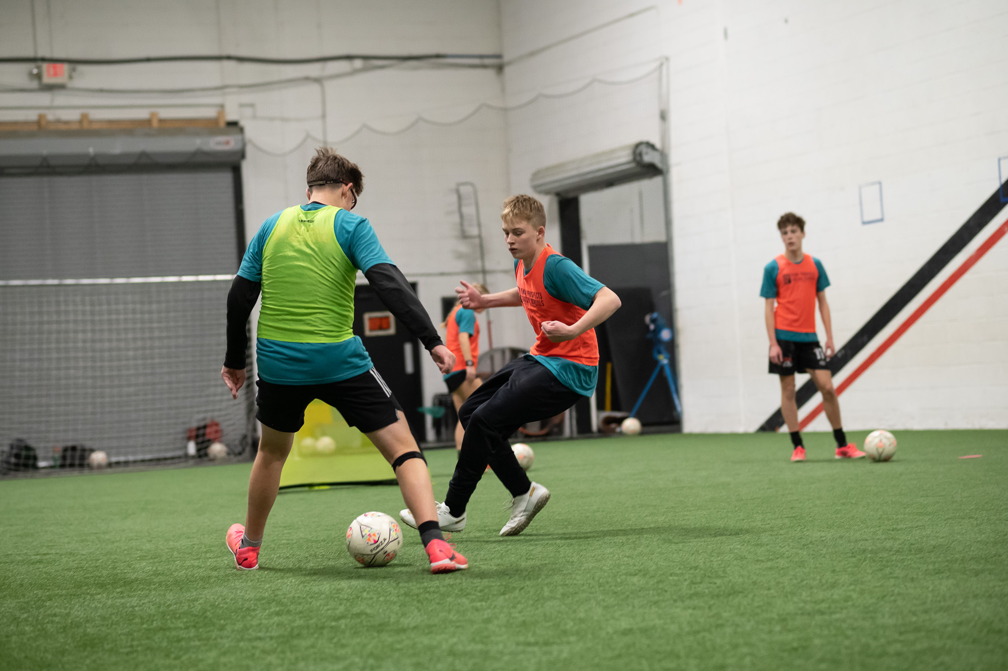 Two young boys playing soccer on a field with other children in the background.