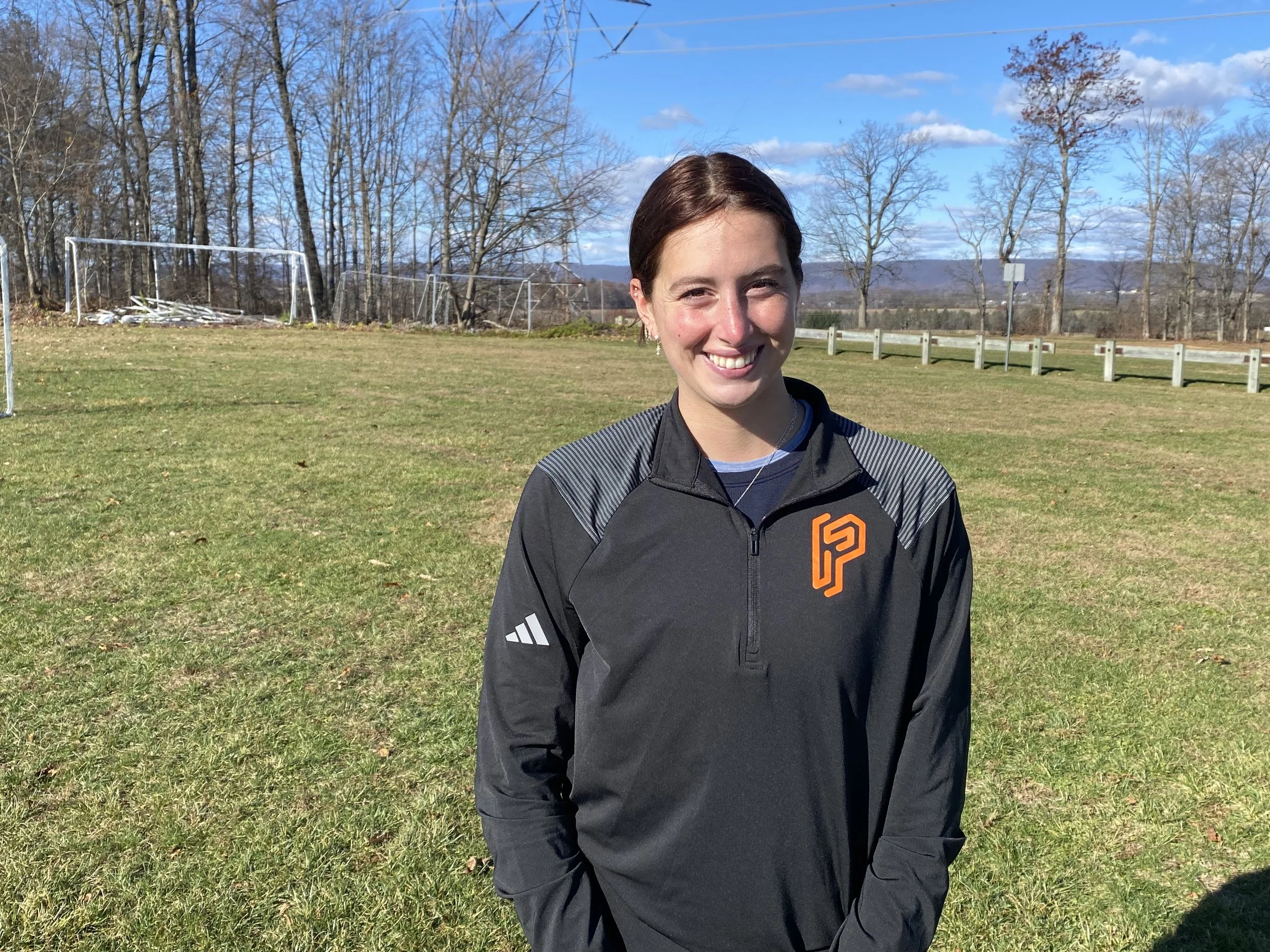 Two young boys playing soccer on a grass field wearing colored bibs, one in orange and the other in green, with a coach nearby.