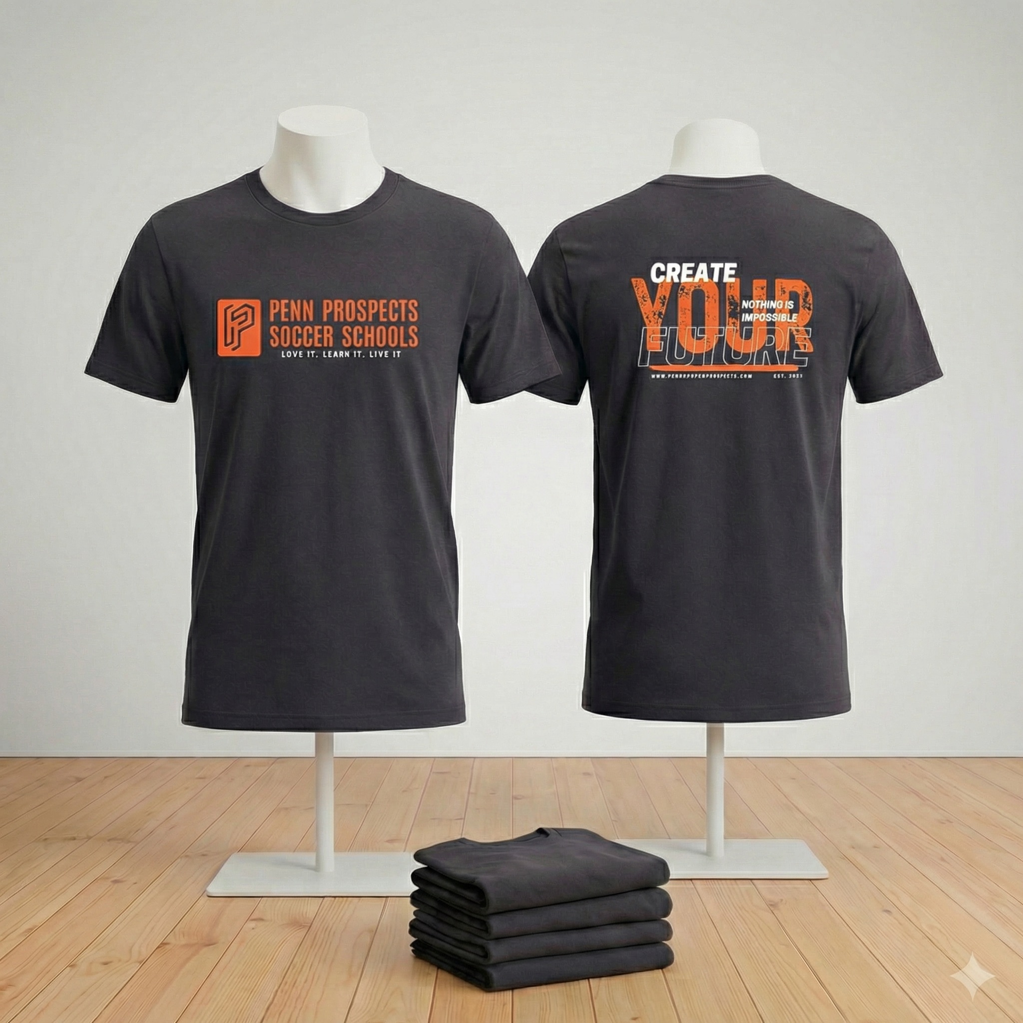 Front and back views of a black T-shirt with orange text for Penn Prospects Soccer Schools; front reads 'Penn Prospects Soccer Schools Love it. Learn it. Live it' and back says 'Create Your Future Nothing is Impossible'.