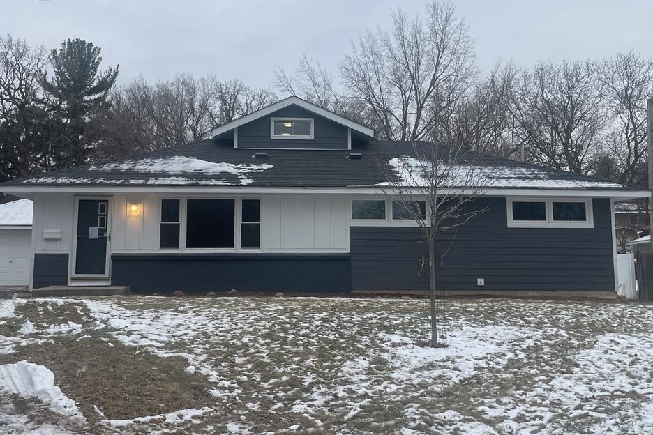 A photo of a house after new siding has been installed, showing dark gray LP SmartSide siding with white trim around the doors and windows and white board & batten vertical siding for accents
