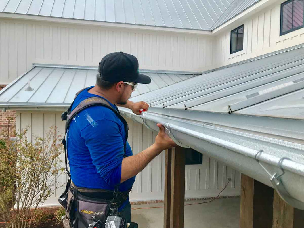 A worker installing seamless aluminum gutters on a home