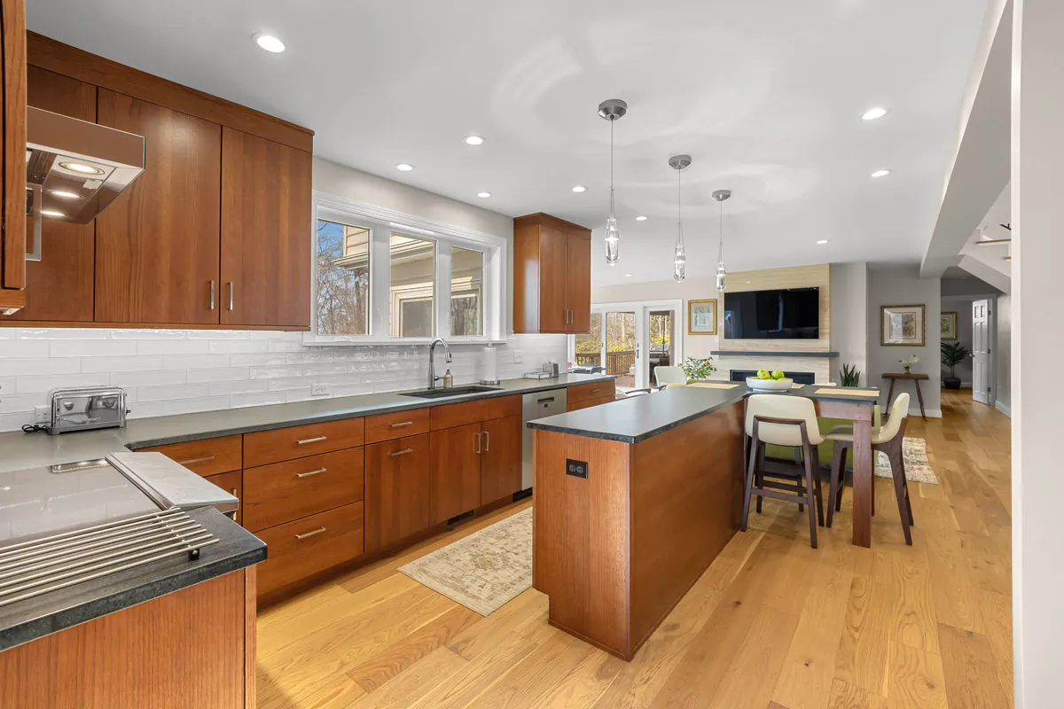Modern open kitchen with wood cabinets, large island, and open dining area leading to living room