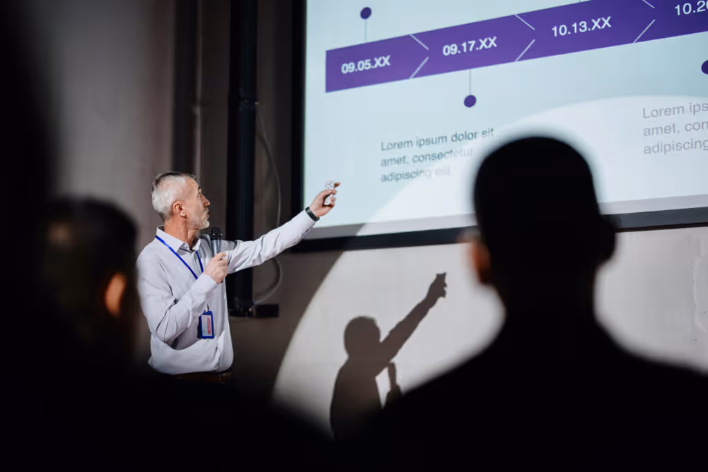 Successful male speaker presents on stage, uses remote control for presentation Showing Infographics