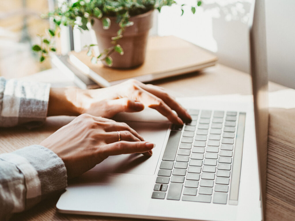 Woman working at home office hand on keyboard. Home workspace - wooden table laptop. Beautiful workspace - online remote work from home concept. close up