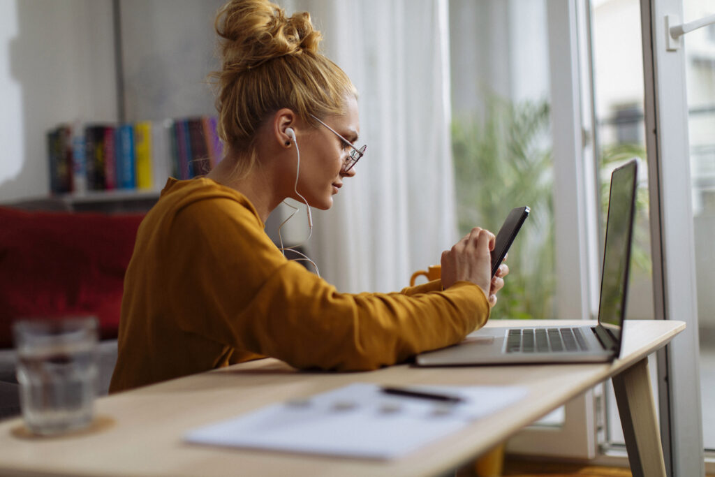 Young blond woman using her cellular phone while working from home