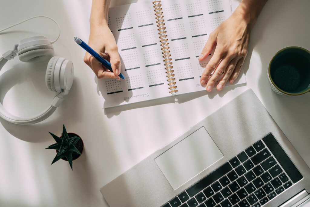 Workspace with laptop and humans hands, white background. Calendar in planner.