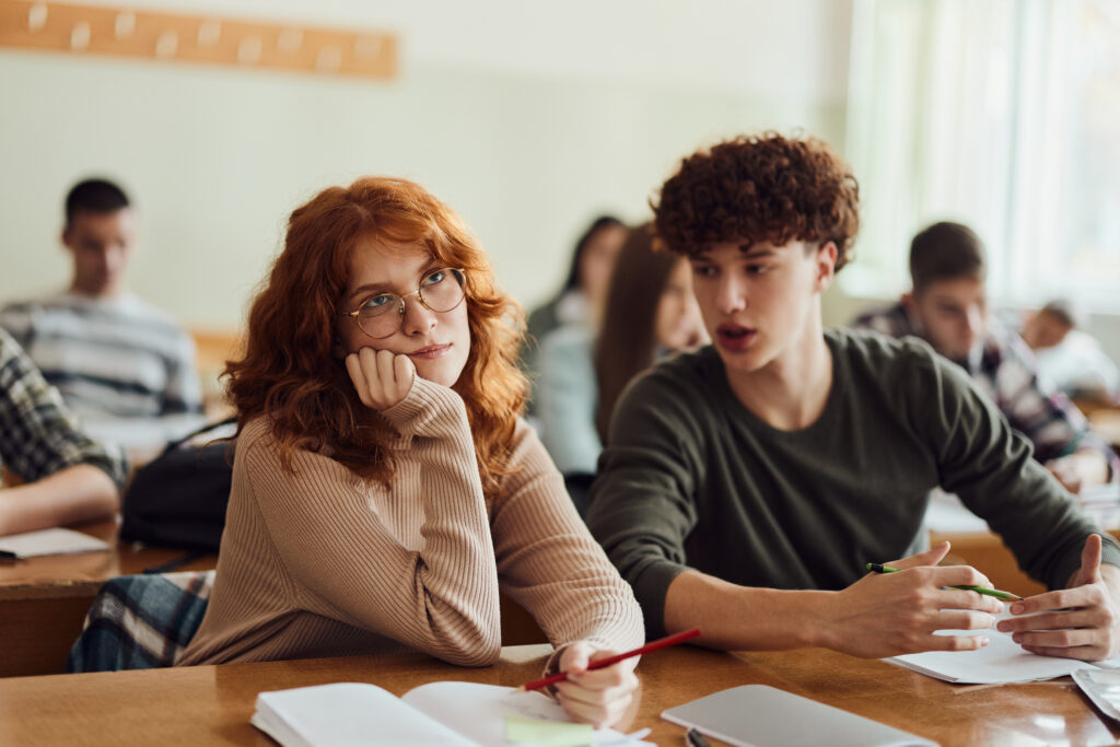 Careless female student ignoring her friend who is talking to her during a class in the classroom.