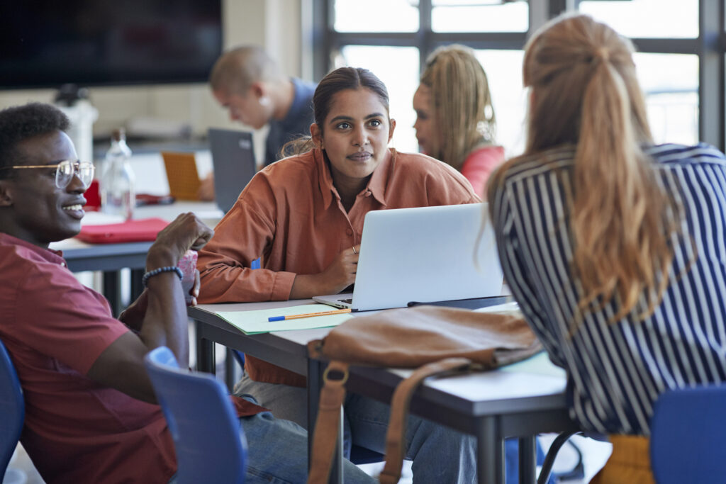 Young man and woman looking at female university student while discussing in classroom