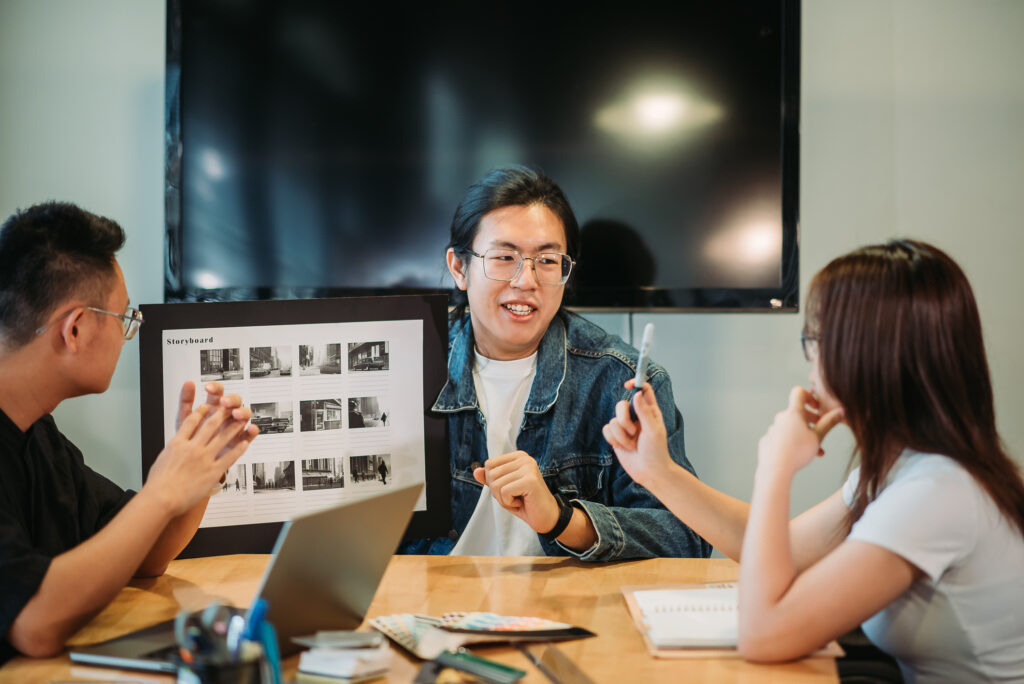selective focus of young man with long hair hand holding storyboard having discussion with team