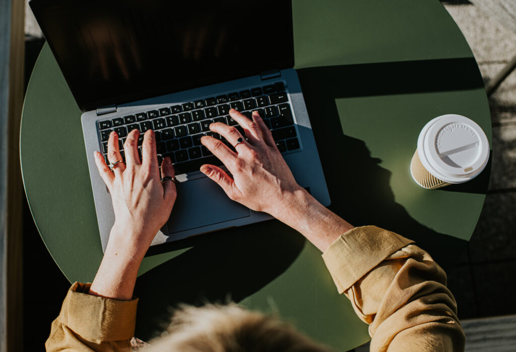 Corporate image of hands typing on a laptop keyboard in an outdoor environment, perhaps a balcony, a garden or a rooftop terrace.