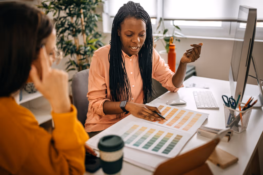 Female colleagues analyzing presentation color swatches while discussing business ideas on desk in small office