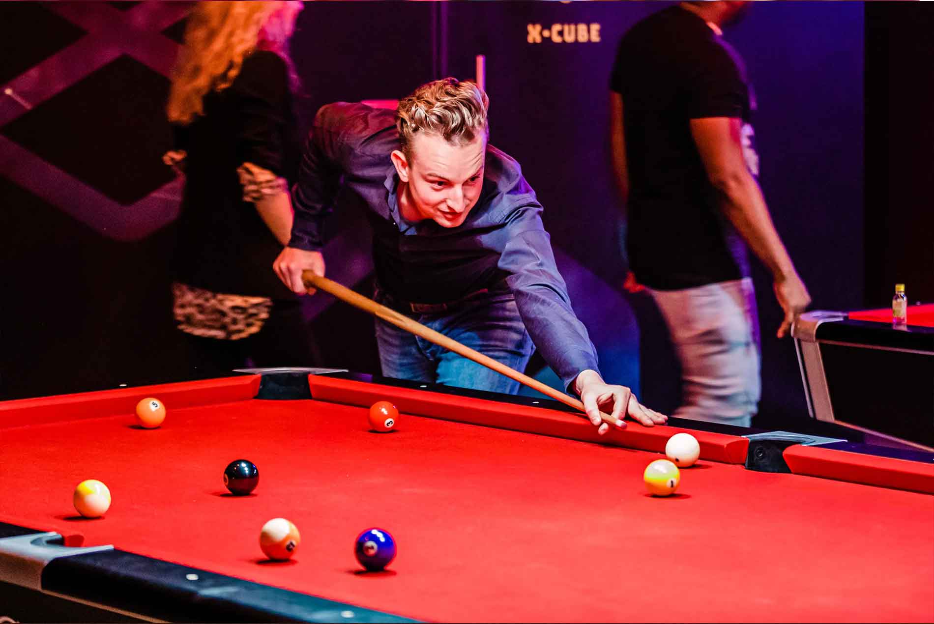 Man in a dark shirt leaning over a red pool table preparing to strike a cue ball with a pool cue.