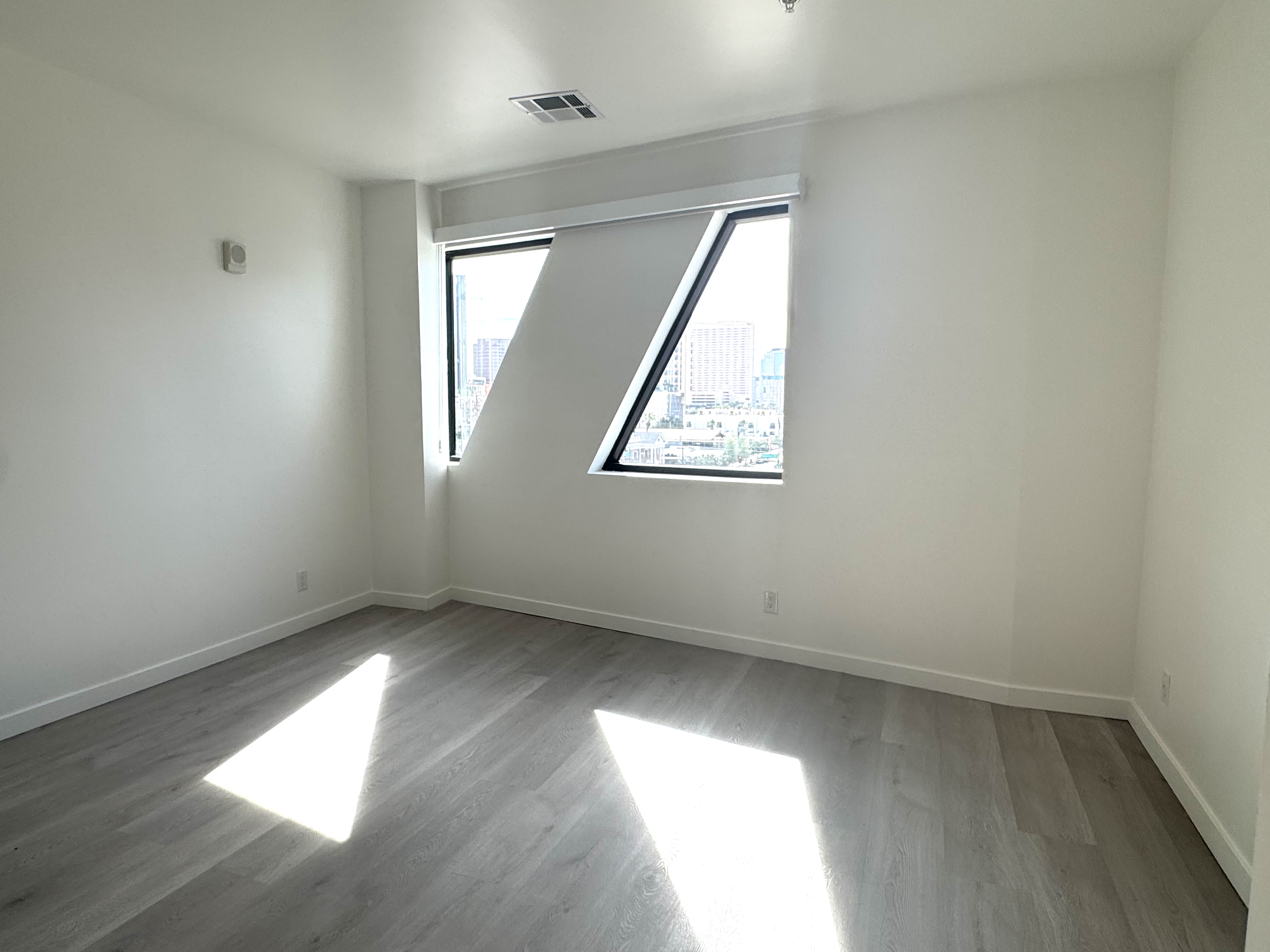 Spacious bedroom with white walls and large windows offering city views from an apartment at Rainbow Road in Phoenix, AZ.