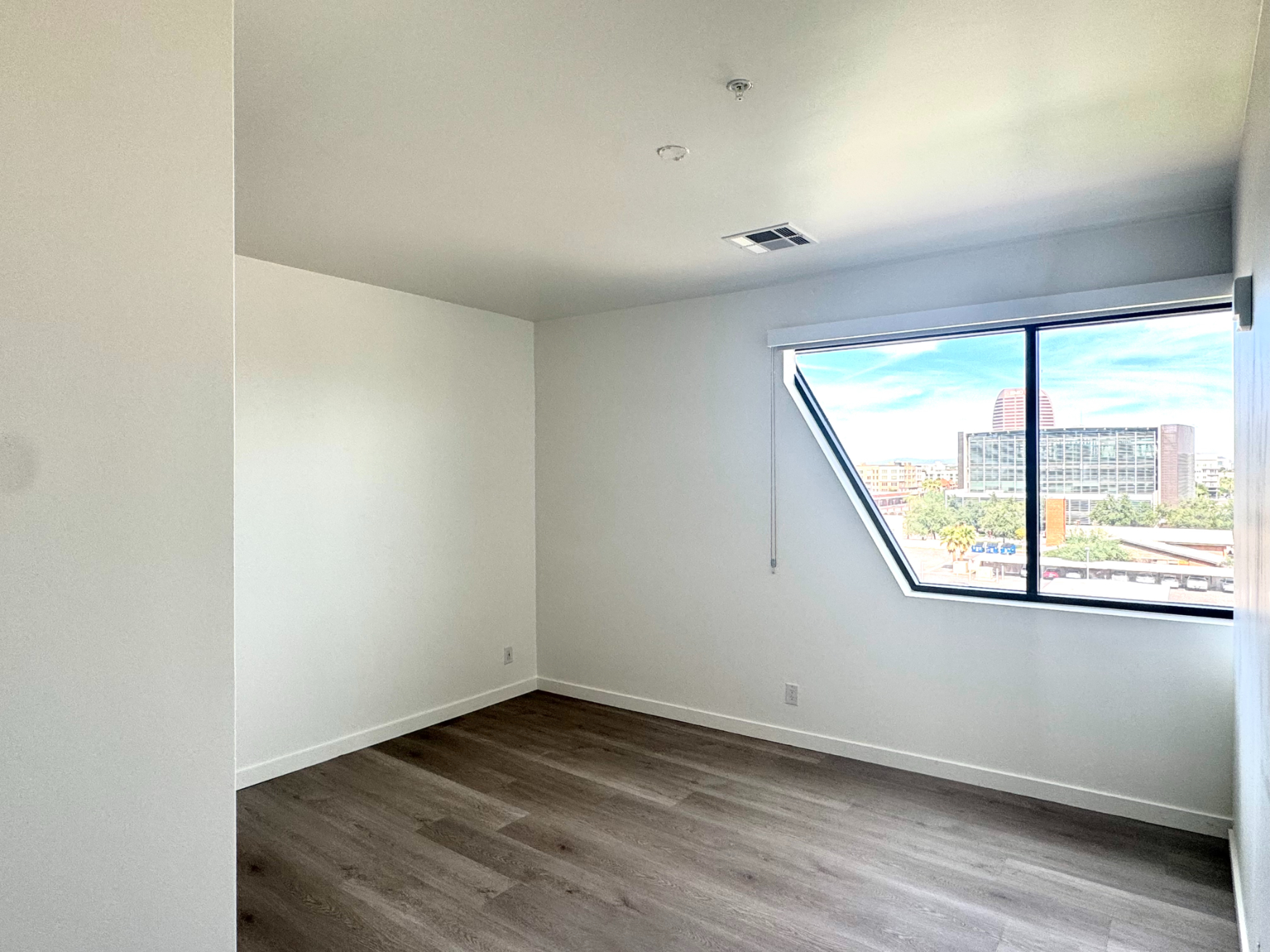 Spacious bedroom with white walls and large windows offering city views from an apartment at Rainbow Road in Phoenix, AZ.