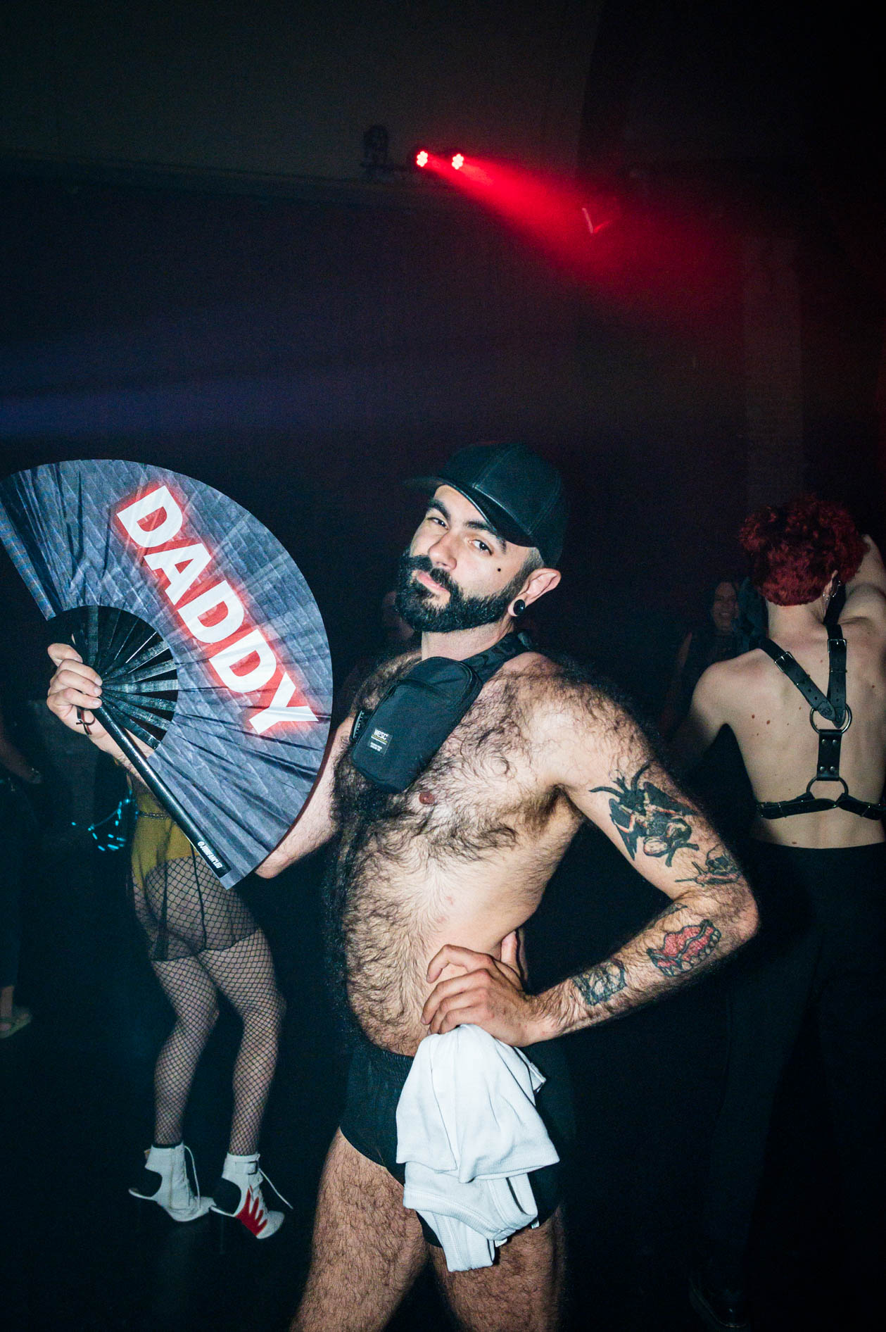 a party goer wearing very little clothing poses with a DADDY fan in downtown Portland