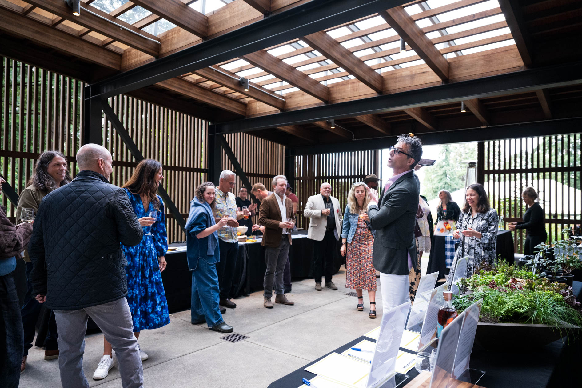 Guests mingle and laugh in a modern, wood-framed pavilion at the Feast in the Garden event in SE Portland. The gathering captures the social and celebratory atmosphere of the private event.