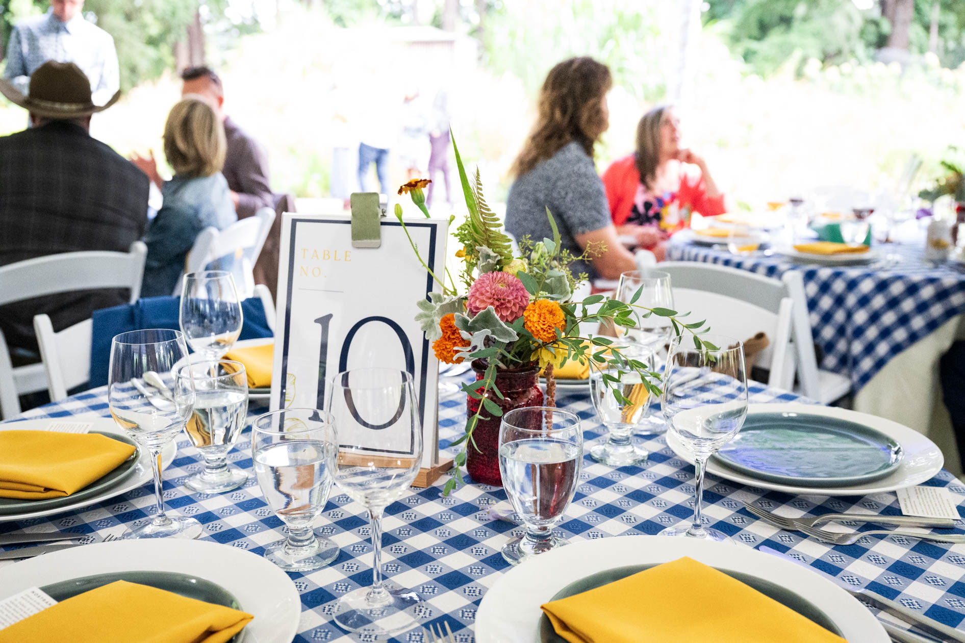 A close-up of a dining table with a checkered tablecloth and flowers, capturing the intimate atmosphere of a meal at the Feast in the Garden event in SE Portland.