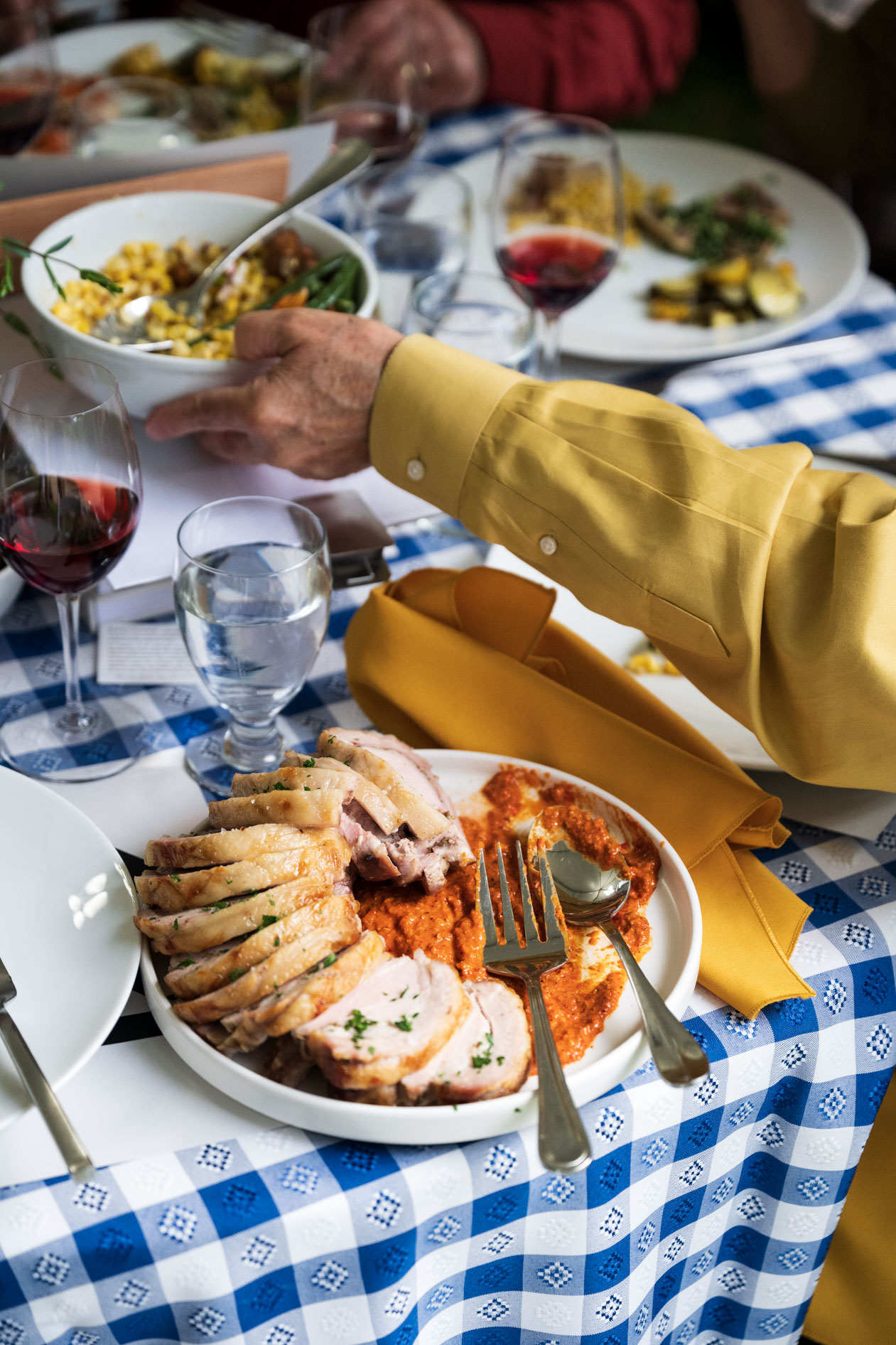 A close-up of a beautifully plated meal, with slices of pork loin on a bed of red sauce, served at the Feast in the Garden event. The dish is on a blue and white checkered tablecloth, capturing the delicious food and elegant dining experience.