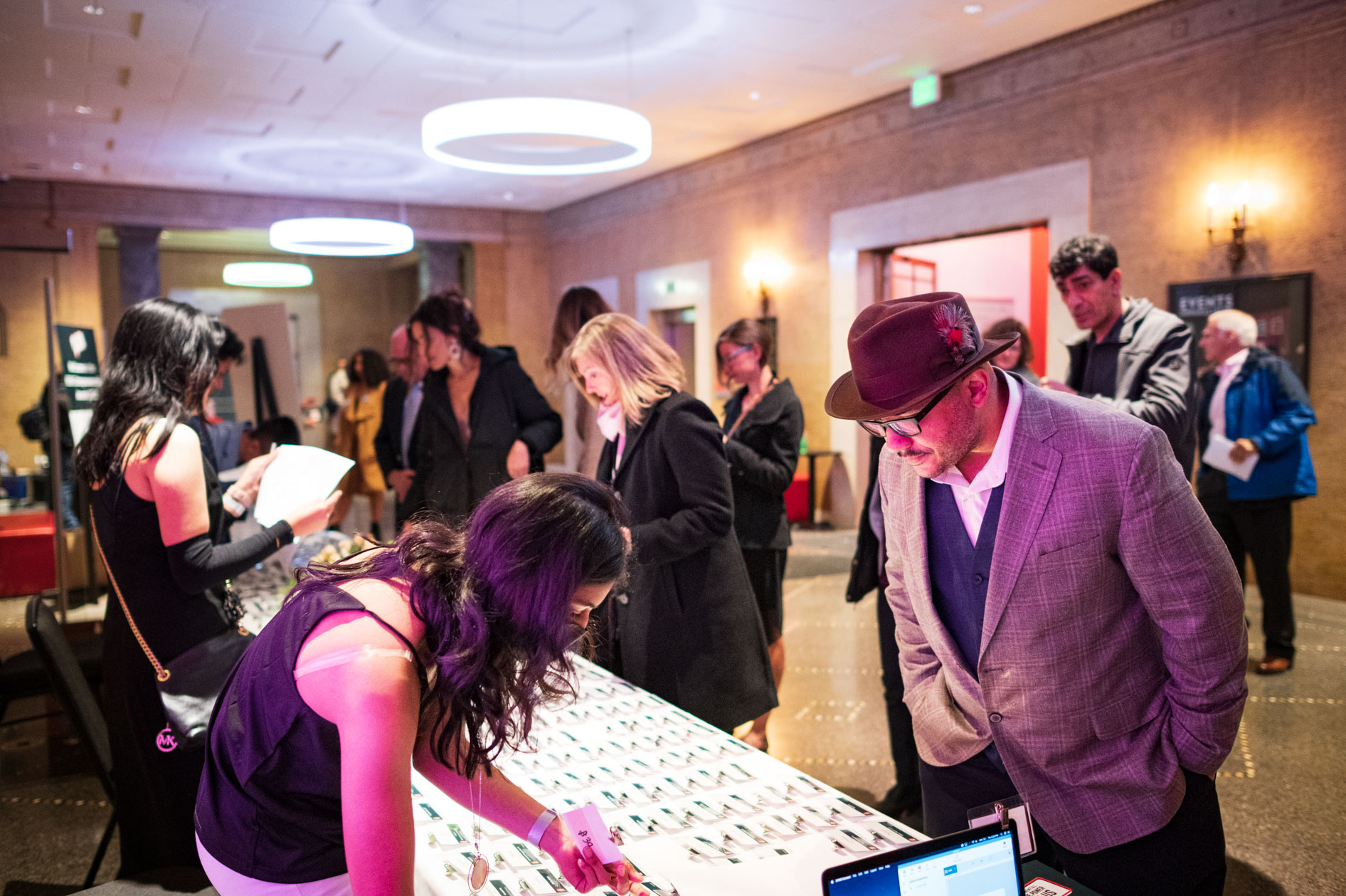 Guests mingle at a check-in table in the grand lobby of the Portland Art Museum. A man in a hat looks down at the table, capturing a moment of quiet focus amidst the lively atmosphere of the OEN Awards 2022.