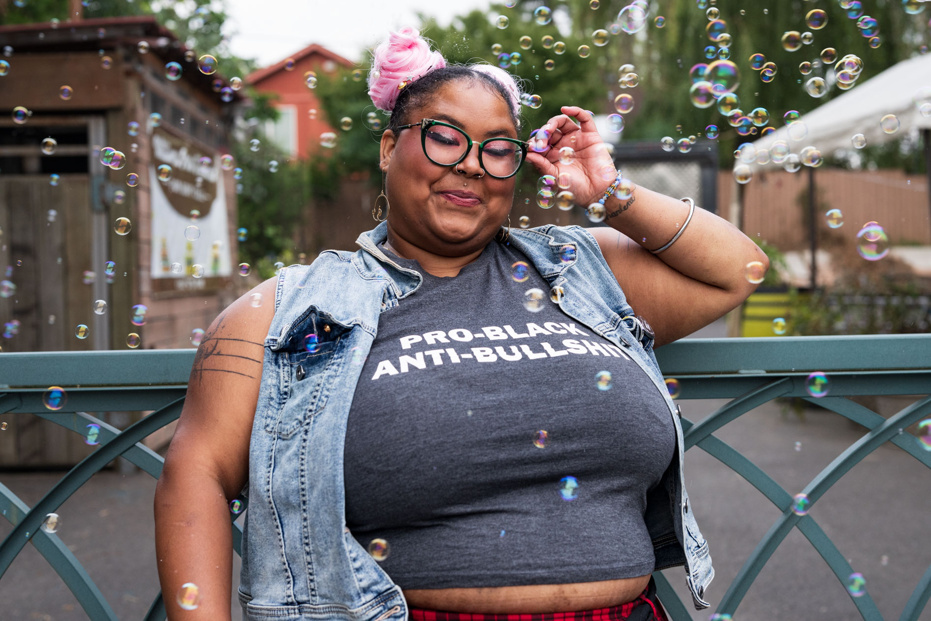 A joyful commercial portrait for a case study with Affect's 'Disabled and Here' series. A smiling trans and disabled person with pink hair and glasses is surrounded by bubbles. This showcases inclusive photography for a T4T pride campaign in Portland, Oregon.