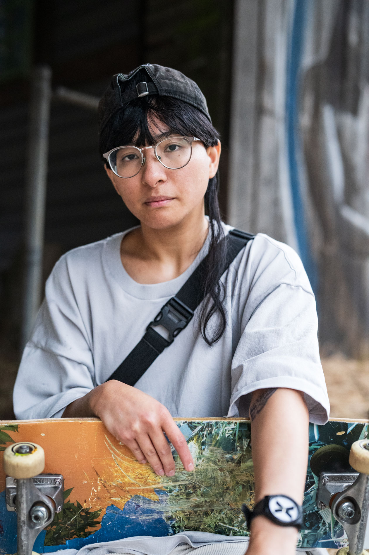 A commercial portrait of a person with a skateboard, wearing a hat and glasses. This is for a case study with Affect's 'Disabled and Here' series, featuring a trans and disabled model in Portland, Oregon.