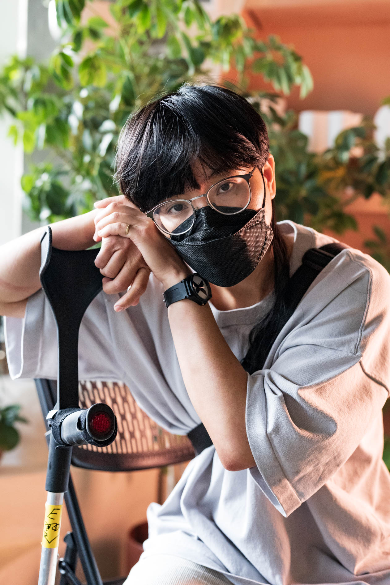 A commercial portrait of a person wearing a mask and glasses, seated with a crutch resting nearby. This image is for a case study about a T4T pride photoshoot for Affect, featuring a trans and disabled model.