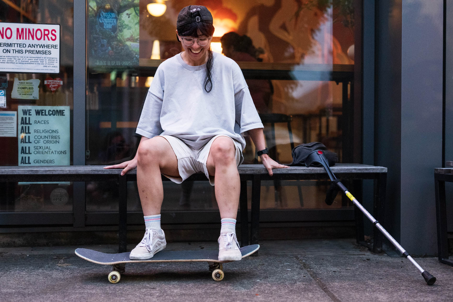 An authentic portrait for Affect's 'Disabled and Here' series, showcasing a person with a skateboard and a crutch, to highlight trans pride and joyful self-expression.