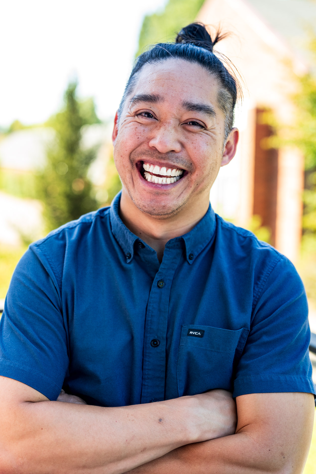 A smiling professional with a bun and short hair on the sides, posing with their arms crossed. This is an example of an inclusive headshot captured for Willamette University in Salem, Oregon.