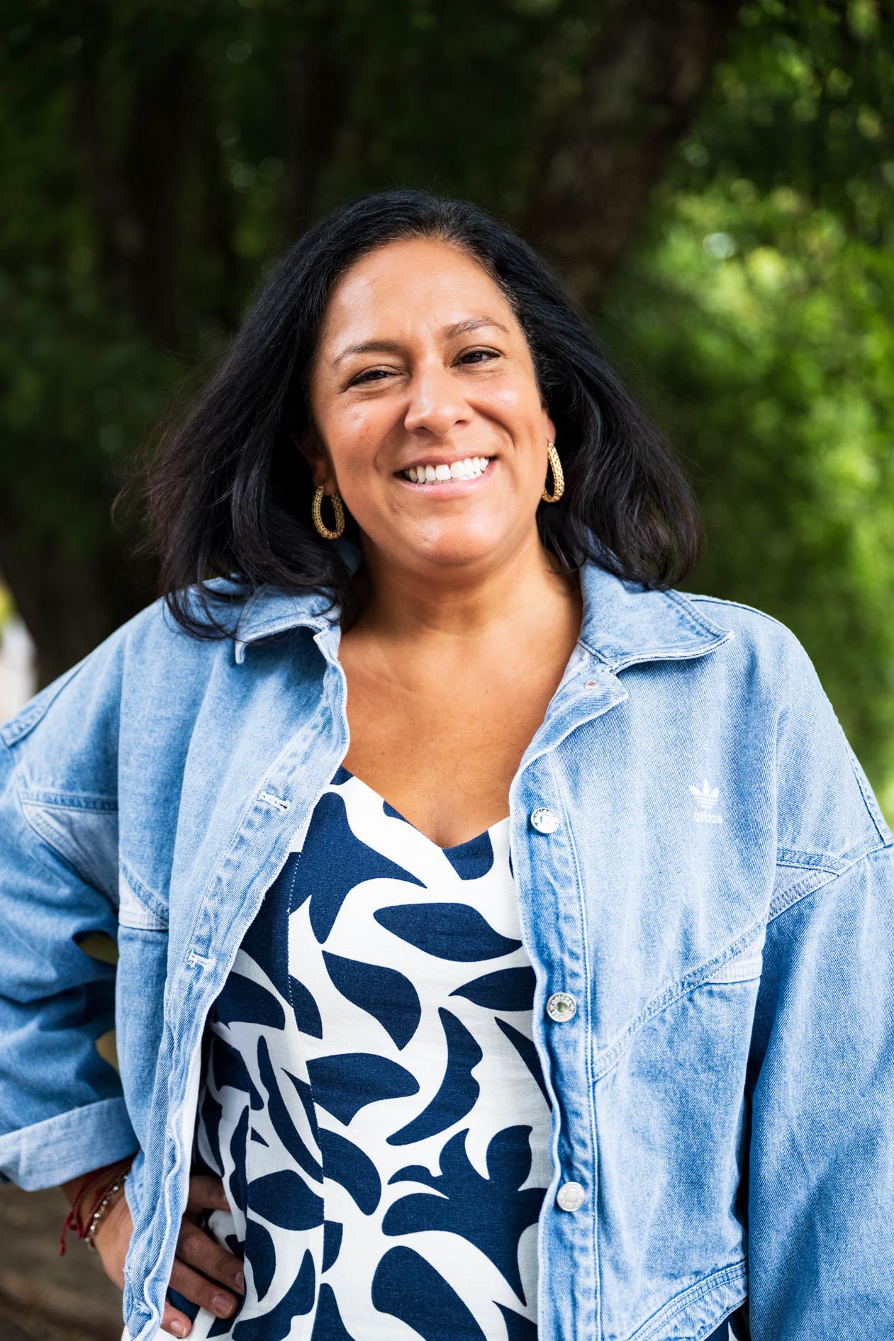 A professional and authentic portrait of a smiling person with dark hair, wearing a denim jacket and a patterned top. This is an example of commercial photography for a business coaching company in Portland, Oregon.