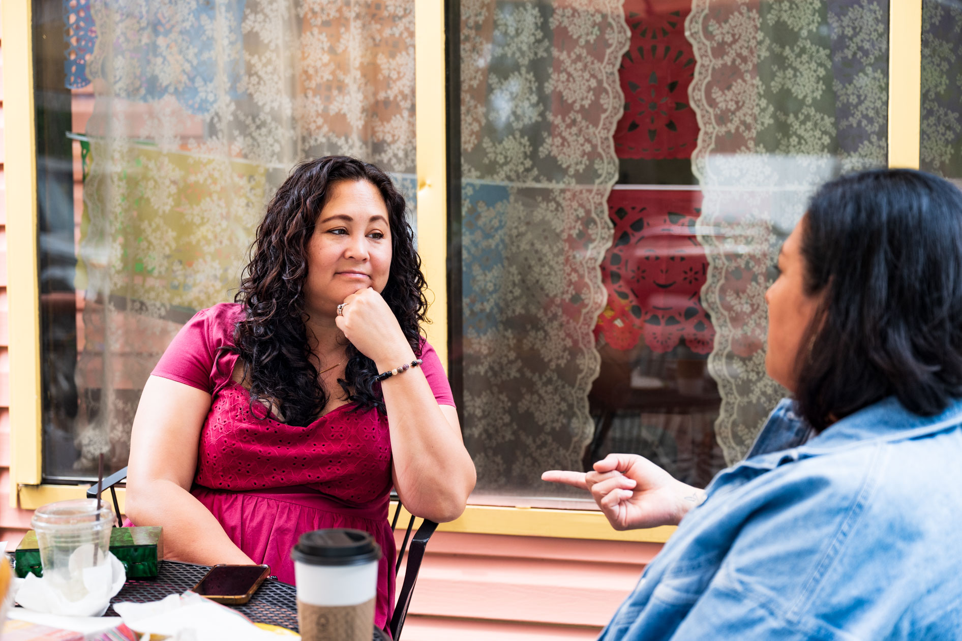 A candid photograph of two colleagues sitting at an outdoor cafe table, talking and laughing. This is an example of commercial photography for a business coaching company in Portland, Oregon.