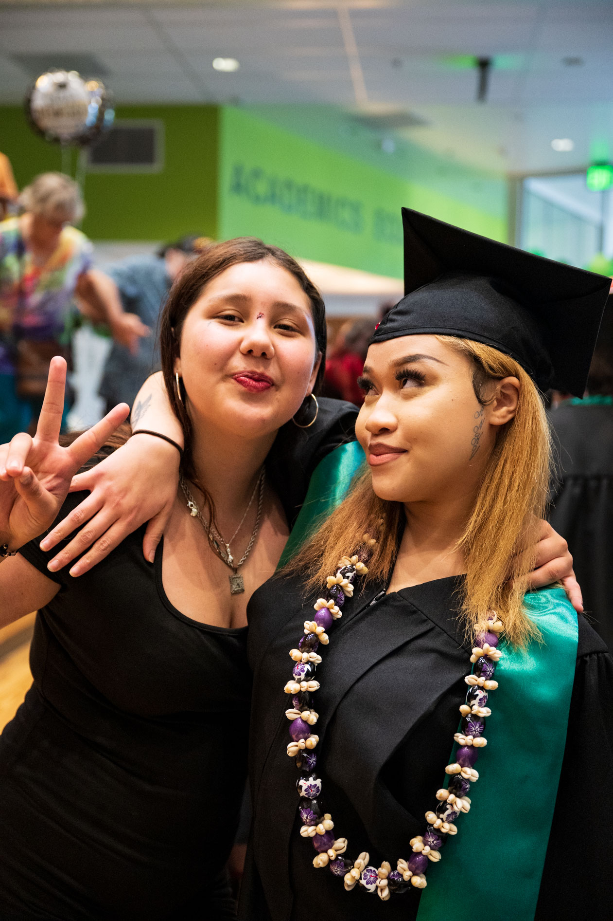 A graduate in a cap and gown with a friend, posing for a photo with a peace sign. This is an example of a Portland event photographer capturing a celebratory moment for Open School East.